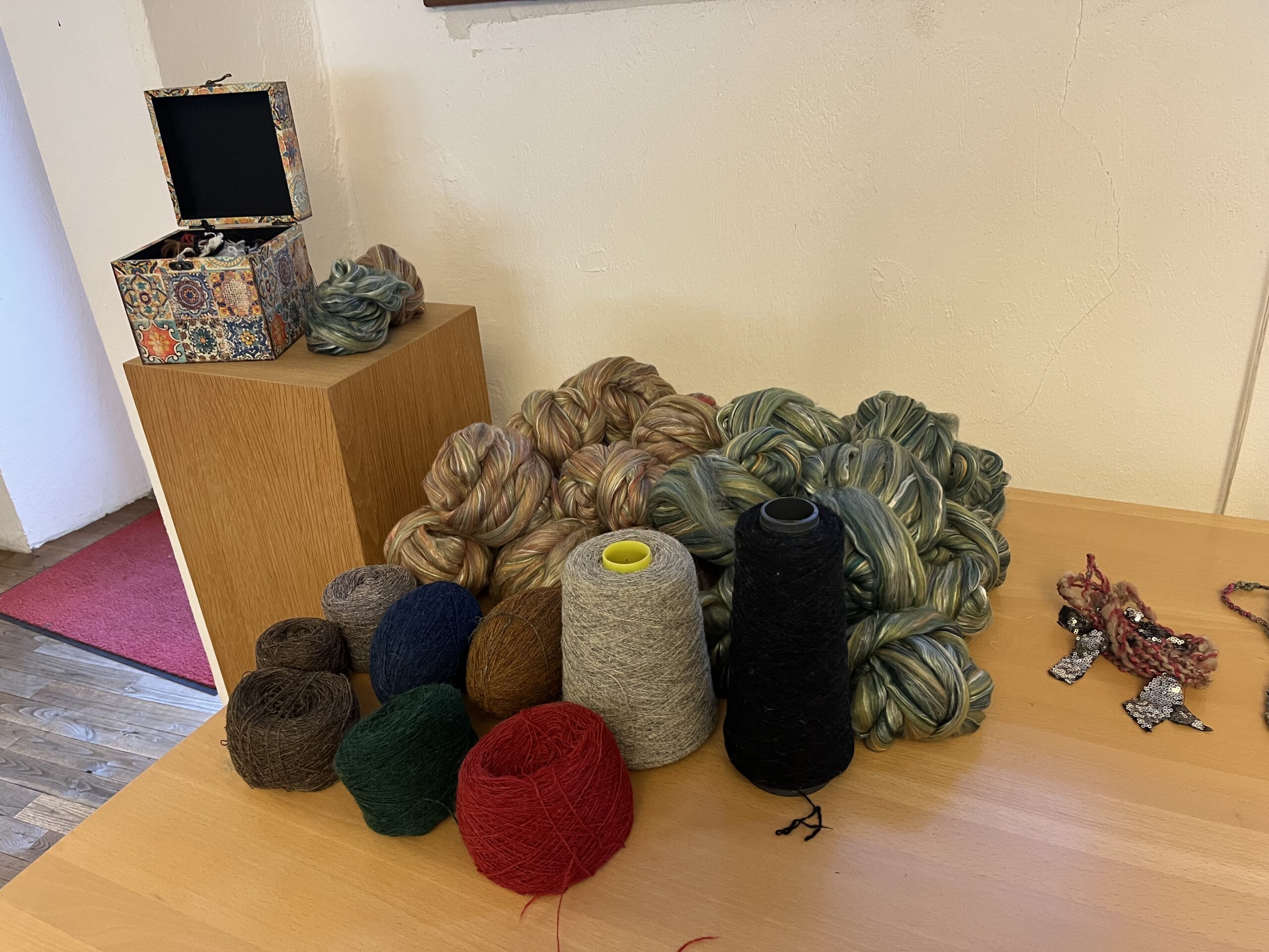 Assorted skeins of yarn in red, green, gray, and brown on a wooden table with a decorative box in the background.