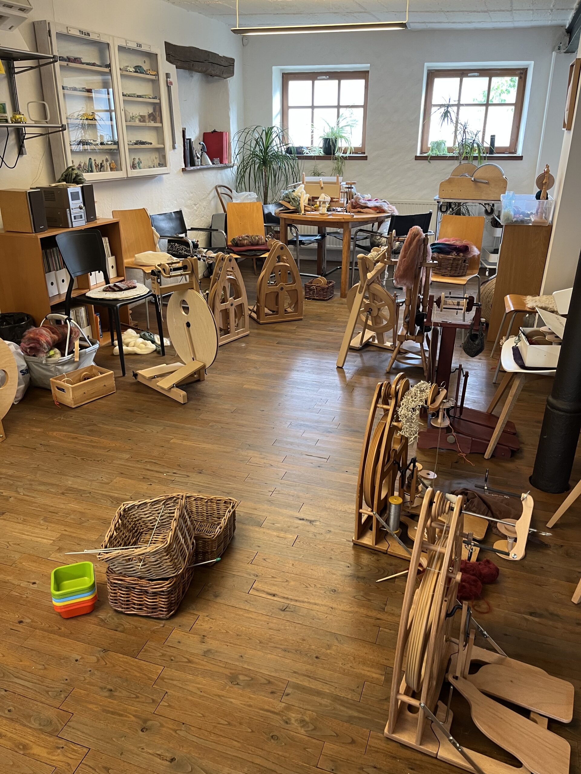 Cozy craft studio with weaving looms, spinning wheels, yarn baskets, and wooden tables organized for fiber arts