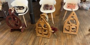 Fiber arts workspace with white chairs, spinning wheels, and baskets of yarn on a wooden floor.