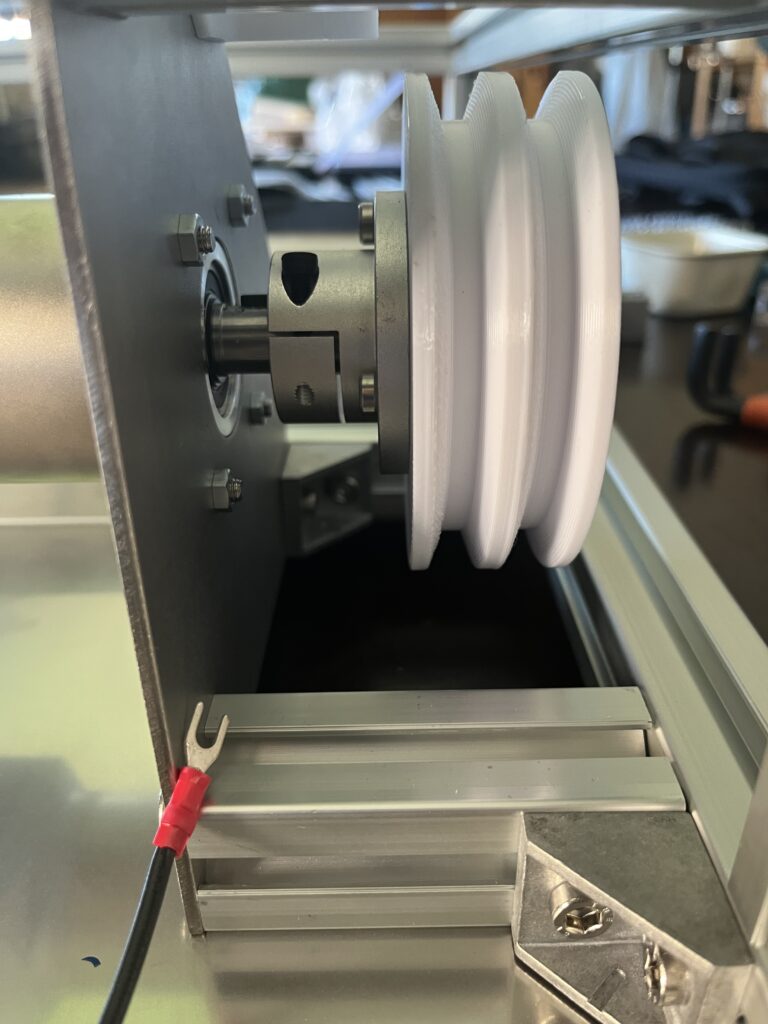 Close-up of a white plastic spool mounted on a metal drive hub inside industrial equipment.