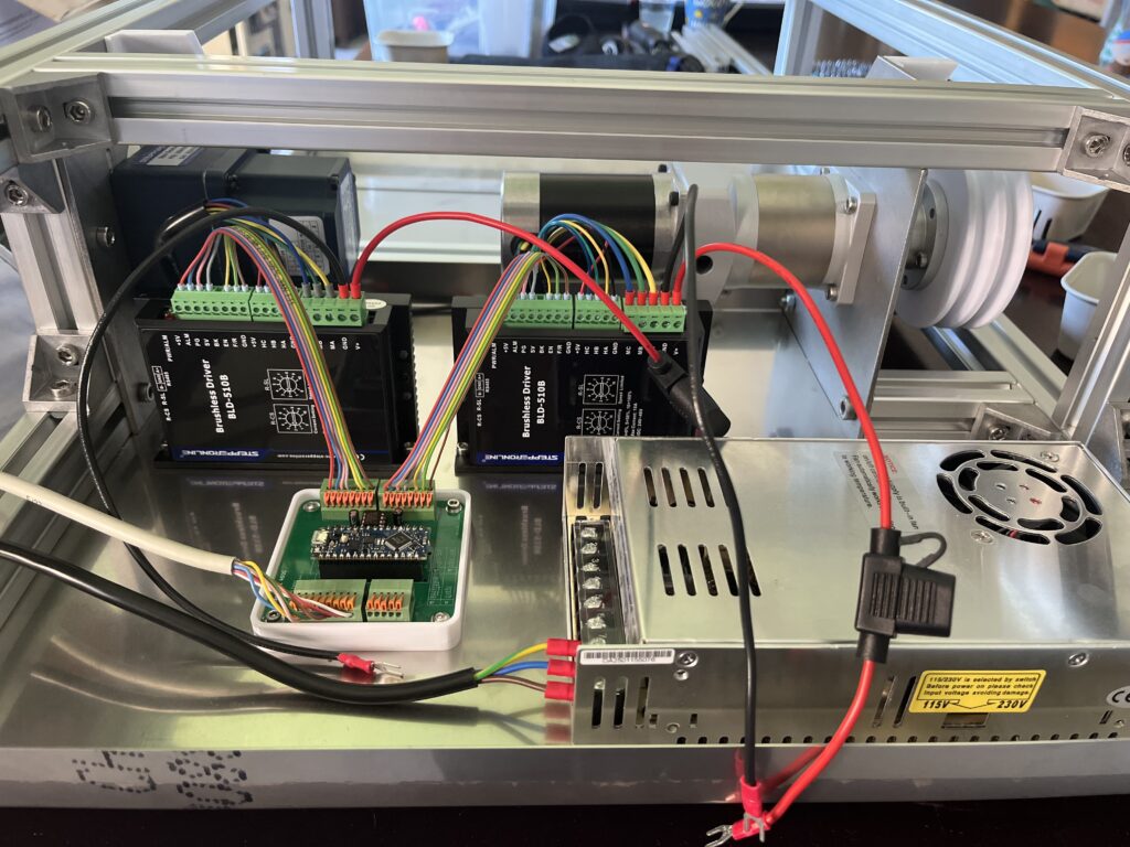 Inside panel of a metal enclosure showing two brushless motor drivers with color-coded wires and green terminal blocks.
