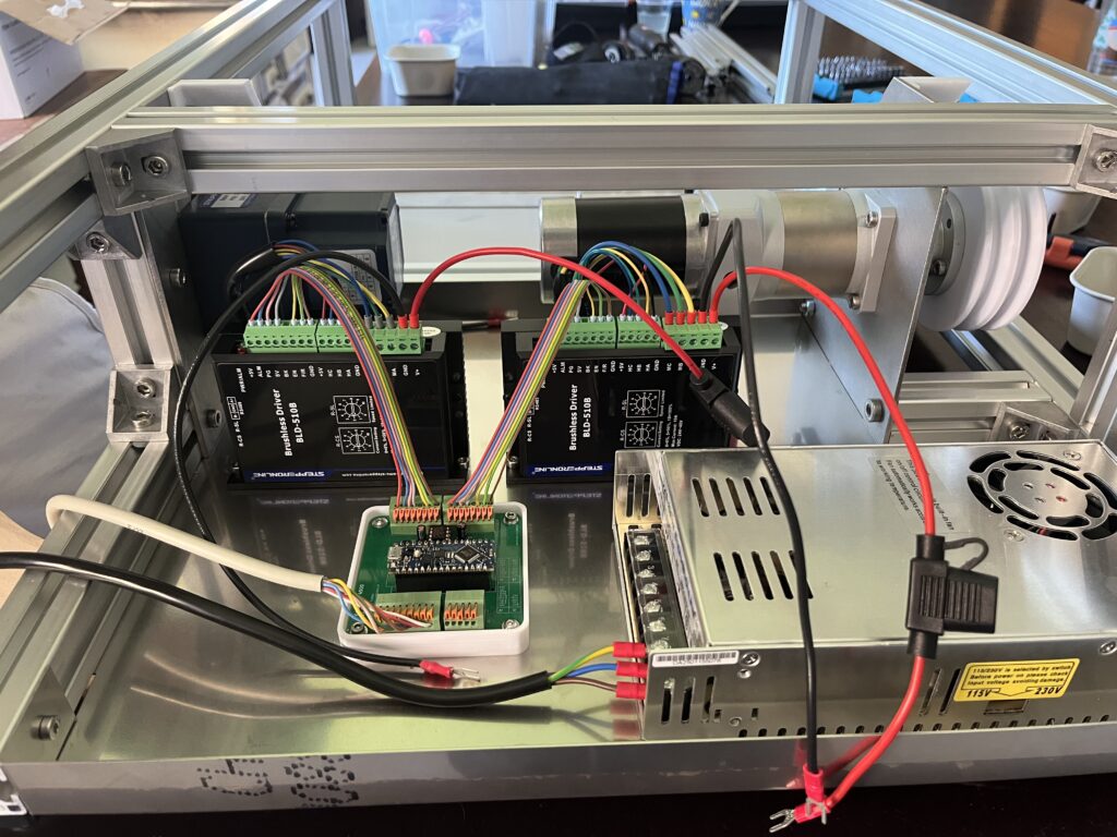 Open electronics cabinet showing brushless driver modules, colorful wire harnesses, and terminal blocks mounted on an aluminum frame.