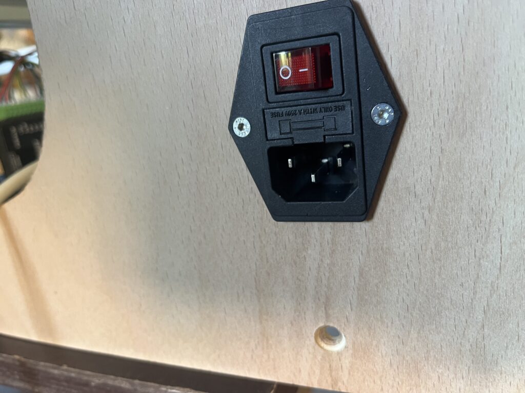 Black wall outlet with a red toggle switch mounted on a tilted rectangular plate and two screws visible on either side of the plate.