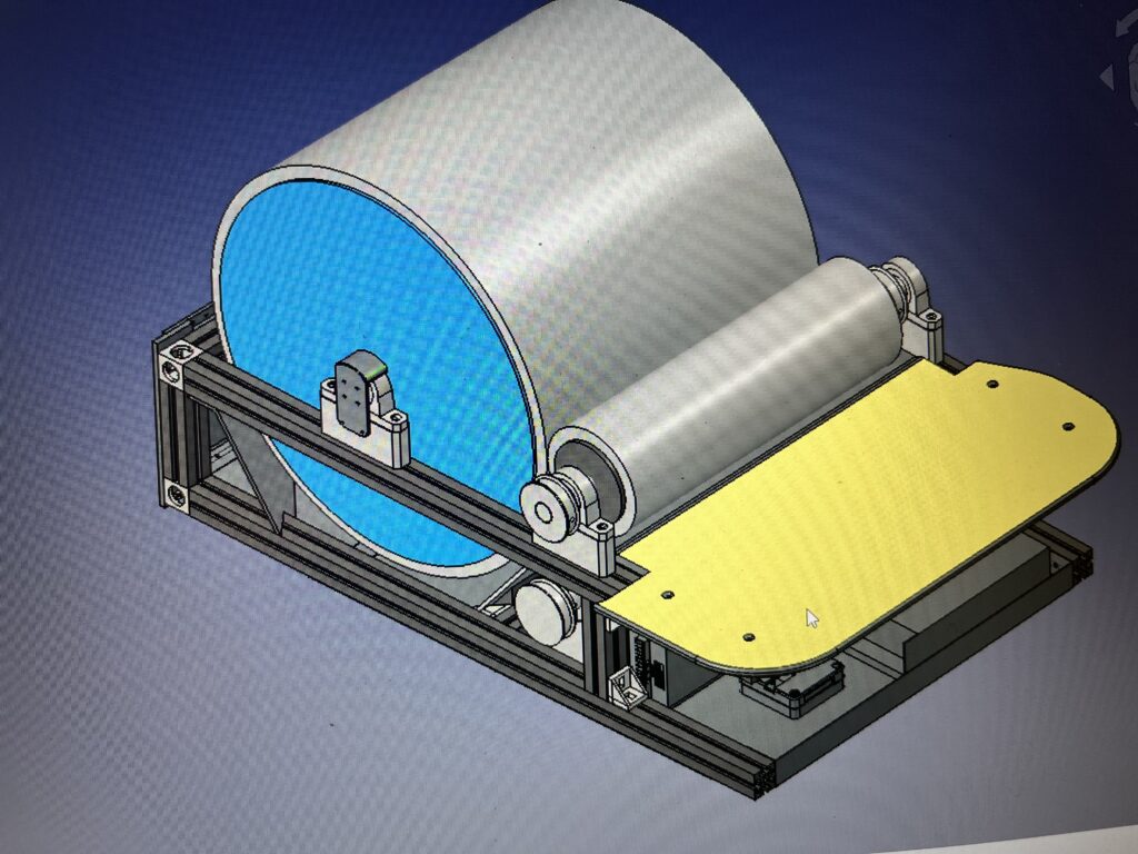 CAD rendering of a large cylindrical roller mounted on a gray frame with a blue end disk and a yellow base platform, viewed from an angled side angle.