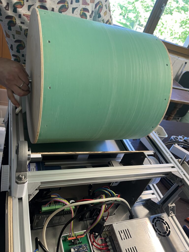 Close-up of a large green cylindrical roller inside an exposed industrial machine with wiring and a control board nearby, suggesting a printer or cutter undergoing assembly or maintenance.