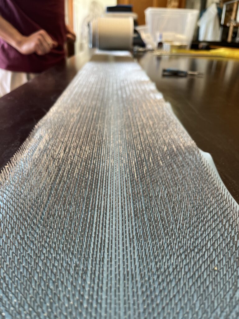 Close-up of a metal bristle mat on a dark countertop with a person in a burgundy shirt blurred in the background.