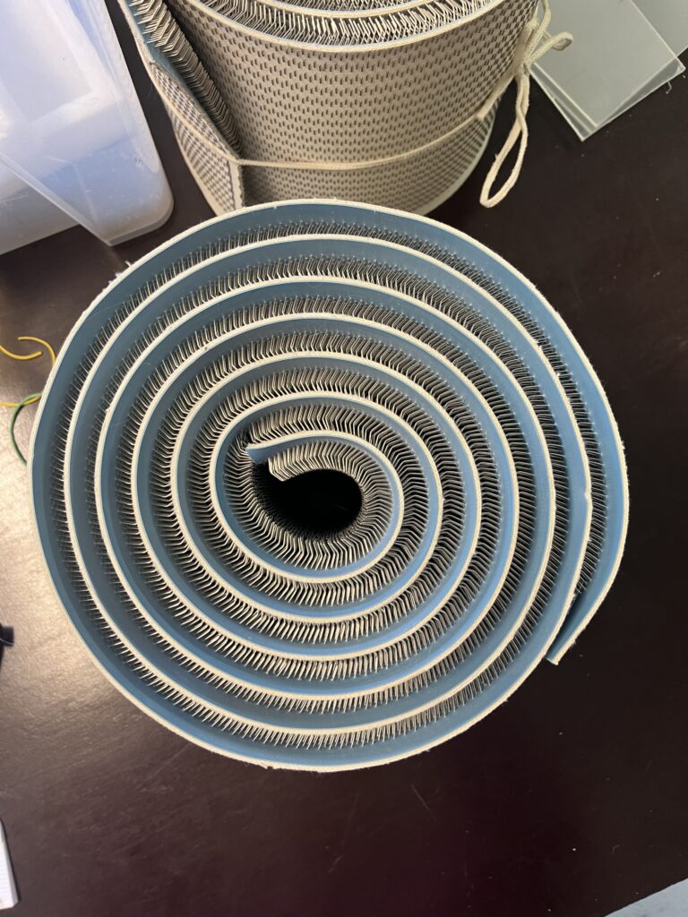 Close-up of blue circular sanding belts stacked in concentric rings with serrated inner edges on a dark table area.
