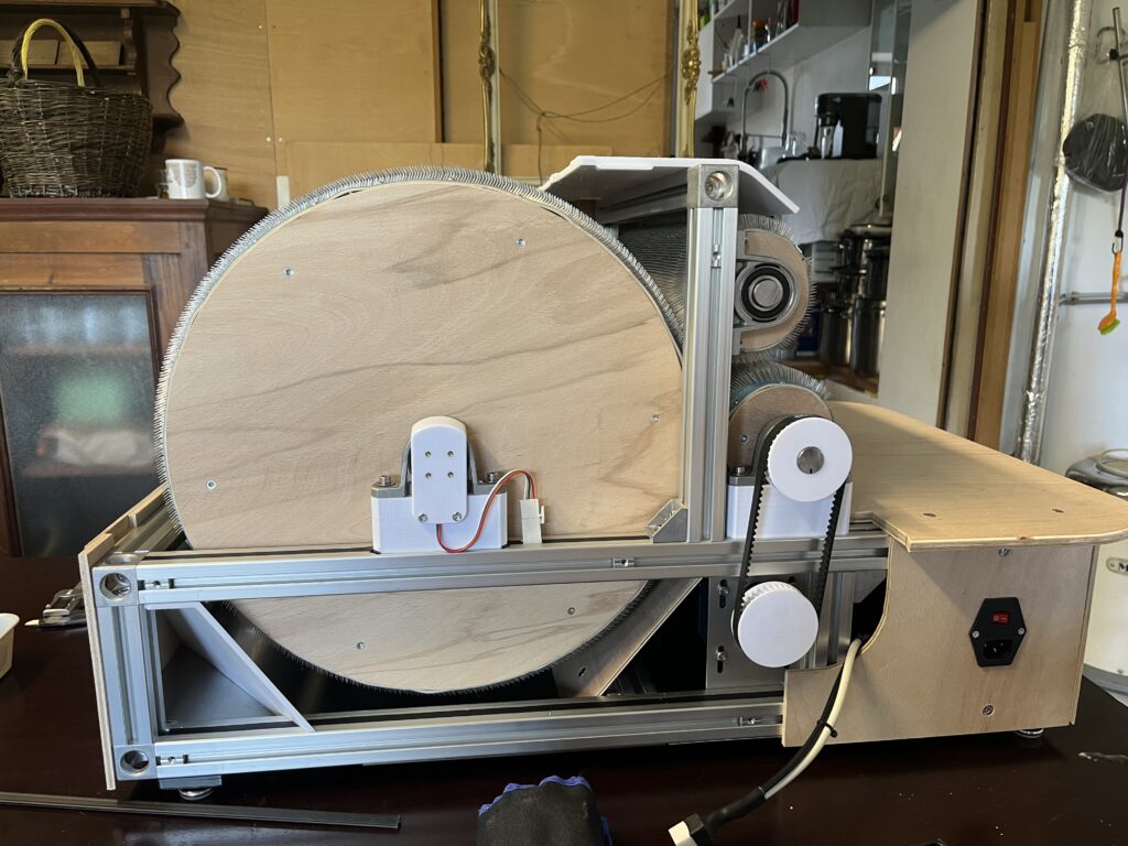 Wooden drum on a metal-frame winding machine in a workshop setting, with belts and gears visible.