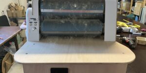 Front view of a Kardomat 4900 industrial roller machine in a workshop, three blue cylindrical rollers with dust and fibers on them.