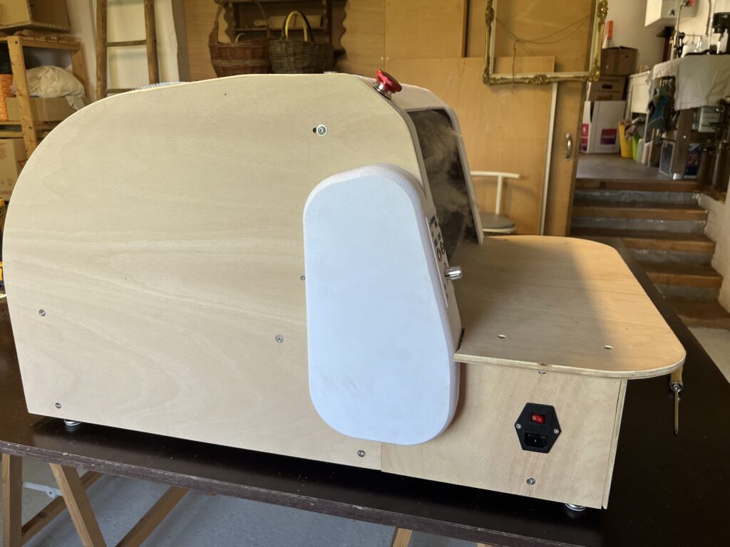Woodworking machine with a curved wooden guard and a red top knob in a cluttered workshop.